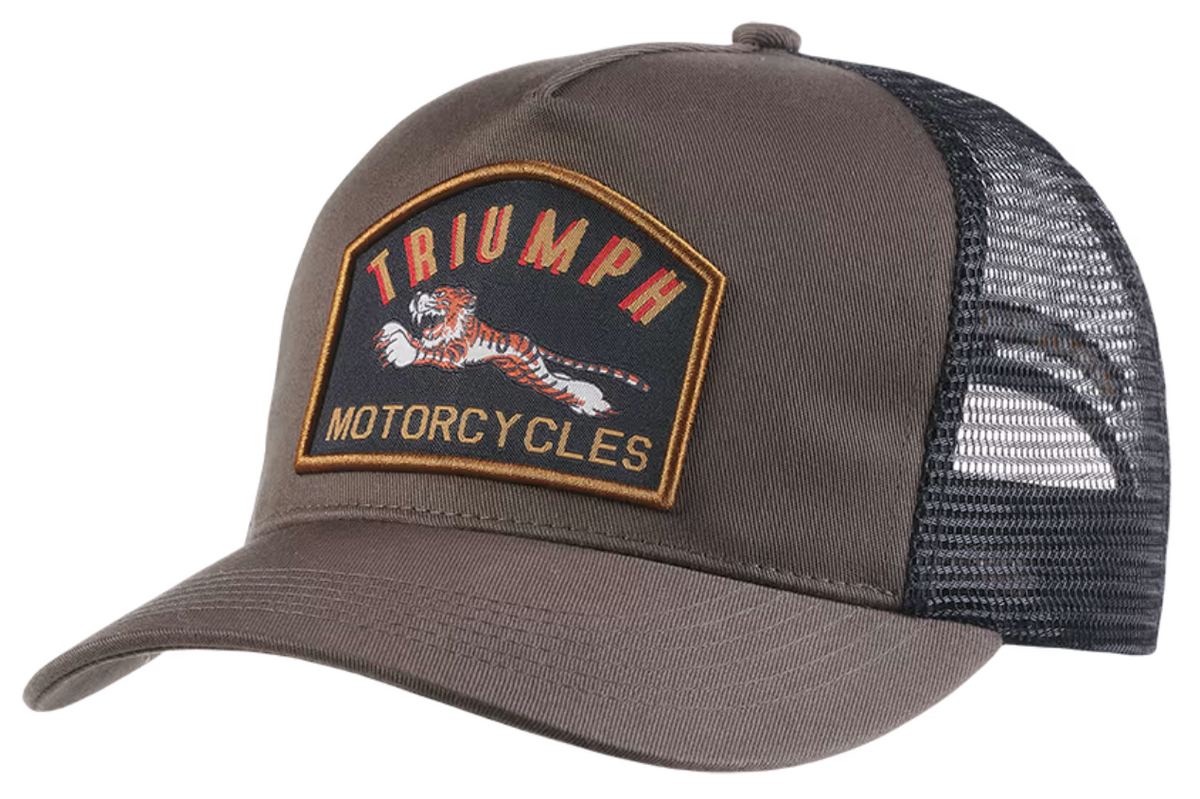 A brown and black trucker hat featuring a prominent embroidered Triumph Motorcycles patch on the front panel, with a curved brim and black mesh back.