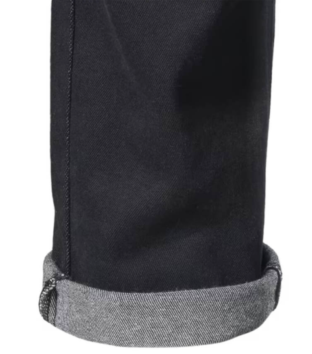 Close-up of the lower leg of dark charcoal gray or black denim pants with a rolled cuff showing a lighter heather gray inner lining, on a white background.